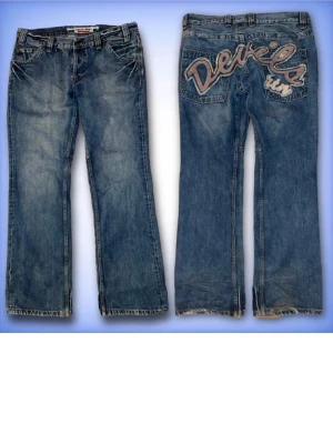 Blå baggy jeans med broderi - Säljer ett par blå baggy jeans med stort broderat 'Devils run' på bakfickorna. Jeansen har klassisk femficksdesign, normal midja och raka ben. Materialet är slitstarkt denim i bomull och passformen är loose för en avslappnad vibe. Innerbenlängd:82cm Ytterbenlängd:108cm                  Midjemått tvärsöver:46cm