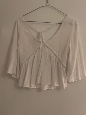 Vit blus med knyt från Hollister XS - Supersöt vit blus från Hollister i tunn bomull med diskreta prickar, v-ringning och öppen rygg med knytband. Säljer pga för liten i byst 💞