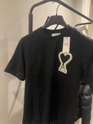 Svart t-shirt från Ami  - En helt ny Svart t-shirt från Ami Paris. Tillverkad i mjuk bomull som känns skön mot huden. Tröjan är i storlek M och sitter perfekt för dig som har bra stil.