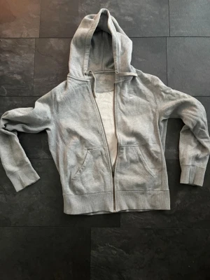 Grå nike zip hoodie Strl S/M - Tja, jag säljer en grå nike zip up hoodie i perfekt skick. Den har en vit logga på bröstet och gråa snören. Inga defekter. Den är i storlek S men jag upplever att den passar M också. Kontakta gärna vid frågor och funderingar.