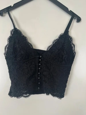 Svart spetsig festtopp  - Säljer en svart korsett-topp från BikBok i storlek XS. Toppen har tunna spetsmaterial med blommigt mönster 