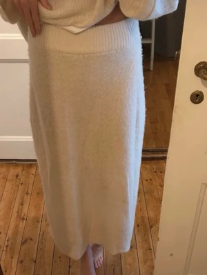 Beige stickad långkjol från Dagmar - Supermjuk och mysig beige långkjol från Dagmar i stickad kvalitet. Kjolen har bred ribbad midja och är gjord av en lyxig mix av babyalpacka, ull och polyamid. Perfekt för dig som gillar en enkel och stilren look med en touch av lyx. Säljer matchande stickad tjocktröja 