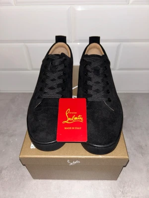 Svarta mockasneakers från Louboutin - Snygga svarta sneakers från Christian Louboutin i mjuk mocka med klassisk röd sula och diskret logga undertill. Skorna har rund tå, svarta skosnören och en stilren, minimalistisk design som passar till det mesta. Insidan är fodrad i beige läder för extra komfort.