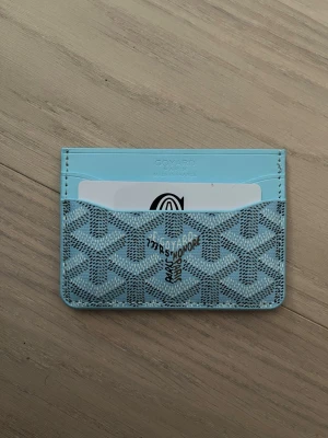 Ljusblå plånbok med mönster - Supersnygg ljusblå plånbok  med deras ikoniska grafiska mönster. Plånboken har flera kortfack och är tillverkad i skinn med tryckt design. Perfekt för dig som vill ha något unikt och stilrent i fickan.