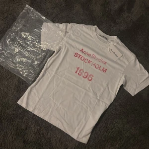  Acne Studios t-shirt Stockholm 1996 - Snygg vit t-shirt från Acne Studios med tryck i rött framtill där det står 'Acne Studios STOCKHOLM 1996'.  