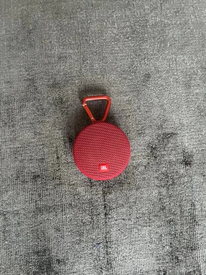 JBL Clip 2 Bluetooth-högtalare - Portabel röd JBL Clip 2 Bluetooth-högtalare med inbyggd karbinhake och 3,5 mm AUX-kabel. Perfekt för utomhusbruk, kompakt och vattentålig design. I mycket bra skick.