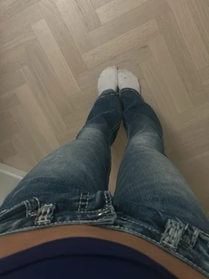 Blå bootcut jeans  - Säljer ett par blå jeans med bootcut-modell och snygga slitningar. Jeansen har mid waist och coola kontrastsömmar, särskilt på bakfickorna där det finns broderade detaljer. Materialet är klassiskt jeans och passformen är normal. Mid waist så jag brukar vika ner de, på bilden ser de lägre ut än vad de är pga att jag vikt ner de litegrann. Använde de 4-5 gånger förra året och köpte på A2 vintage i mos för 850 kr. Storlek 27/32 eller 26/32 inte helt säker.