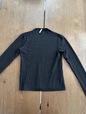 Svart ribbad långärmad topp  - En svart långärmad topp från Nelly med ribbad struktur och rak passform. Nästan som en halv-polo i halsen. Storlek S