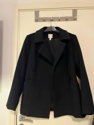 Svart kappa från H&M i ullmix - Stilren svart kappa från H&M i klassisk modell med krage och knäppning framtill. Jackan har två stora fickor och är fodrad på insidan. Perfekt för dig som vill ha en enkel och tidlös look under höst och vinter. Använd fåtal gånger. Pris kan alltid diskuteras!🤗