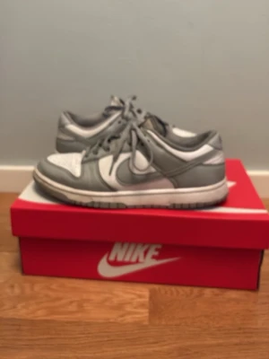 Nike Dunk Low Retro grå/vit sneakers - Nike Dunk Low Retro sneakers i grått och vitt med klassisk låg siluett. Skorna har snörning, rund tå och är tillverkade i skinn och textil. Perfekta för dig som gillar streetstyle och vill ha en ikonisk sneaker i garderoben. Med skolåda 40.5 storlek ganska bra skick med få defekter 