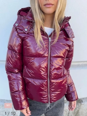 Vinröd glansig pufferjacka med huva - Säljer en vinröd pufferjacka med glansig finish och huva. Jackan har dragkedja framtill och är vadderad för extra värme. Perfekt för kyliga dagar och ger en cool look till din outfit. Nypris på den är 800, och har använt den några fåtalgånger. Men båda knapparna i fickorna har släppt men ingeting som jag märker av💕