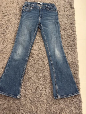 Blå bootcut jeans från Zara - Snygga blå jeans från Zara i bootcut-modell med klassisk femficksdesign och ljusa slitningar framtill. Jeansen har normal passform och är tillverkade i slitstarkt bomullsmaterial. Perfekt för dig som gillar retrovibbar och vill ha ett par jeans med lite extra attityd.