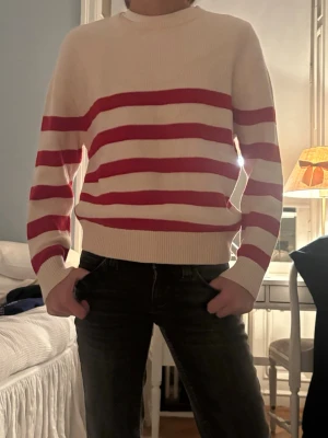 Vit och röd randig stickad tröja - Säljer en vit stickad tröja med breda röda ränder. Tröjan har rund halsringning, långa ärmar och ribbade muddar vid ärmslut och nederkant. Perfekt för dig som gillar en klassisk men ändå färgstark look från Zara .