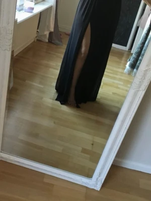 Svart långklänning med paljetter - Säljer en svart långklänning med glittriga paljettdetaljer i silver och guld på överdelen. Klänningen har en hög slits på sidan och ett flowy fall i kjolen. Perfekt för bal eller fest och ger en riktigt glam känsla.