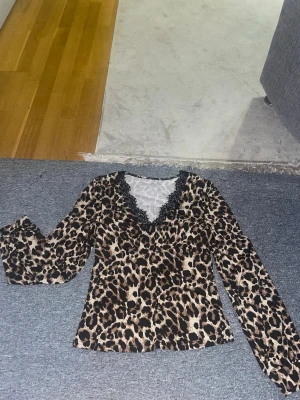 långärmad topp med leopardmönster - En fin långärmad topp i leopardmönster Den har V-nacke med svart spets. Den är från Shein. Tyget är tunt och mjukt. Armarna har resår/elastic längst ner.