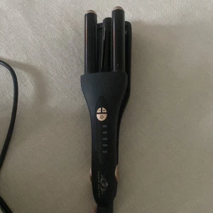 Paris Hilton Triple Barrel Curling Iron - Paris Hilton trippeltång för lockar, med justerbar temperatur (100-180°C). Svart design med roséguldsdetaljer. Ser ut att vara i gott skick utan synliga defekter eller slitage. Perfekt för att skapa voluminösa vågor och lockar.