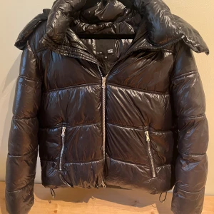 Svart pufferjacka med huva från lager 157 - Säljer en svart, glansig pufferjacka från lager 157 i storlek XS. Helt ny utan lappar 