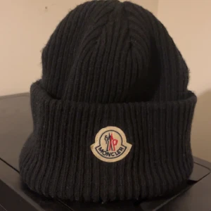 Svart ribbstickad Moncler mössa - Svart ribbstickad mössa från Moncler med klassisk uppvikt kant och broderad logotyp framtill. Går inte ner i pris, Helt oanvänd, kontakta gärna vid intresse😊