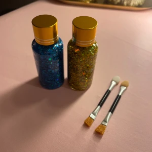Blå och guldig glitterögonskugga + borstar - Två flaskor med chunky glitterögonskugga i blått och guld, perfekt för kreativa sminkningar. Kommer med två dubbelsidiga applikatorer, ena sidan med borste och andra med svamp. Flaskorna har snygga guldiga lock och rymmer mycket produkt.