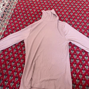 Rosa ribbad polotröja från Amisu XL - Ljusrosa ribbad polotröja från Amisu i storlek XL. Tröjan har lång ärm, hög polokrage och är tillverkad i mjuk viskosblandning med stretch. Perfekt för lager-på-lager och snygg till både jeans och kjol.