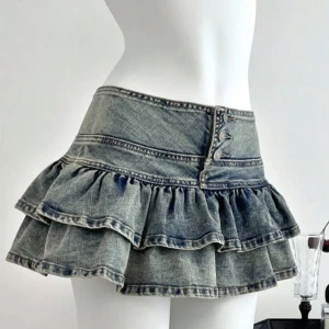Blå lågmidjad volangkjol i jeans med knappar - Supersöt kort jeanskjol i blå denim med dubbla volanger och dekorativa knappar framtill. Kjolen har markerad midja och cool tvättad look som ger en trendig vibe. Perfekt för dig som vill sticka ut med en edgy och lekfull stil❤️❤️.
