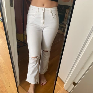 Vita highwaist jeans med slitningar - Säljer ett par vita jeans med hög midja och raka ben. Byxorna har slitna detaljer vid knäna och råa, fransiga benslut för en trendig look. Klassisk femficksmodell i bomull med lite stretch. Perfekta för dig som gillar en clean men edgy stil.