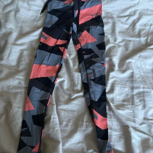 Mönstrade leggings i svart, grått och rosa - Säljer ett par snygga leggings med grafiskt mönster i svart, grått och rosa. De har en tight passform och är perfekta för träning eller chill. Materialet är stretchigt och bekvämt, med bred midja och snörning upptill.