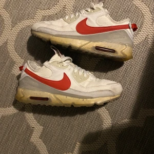 Nike Air Max 90 Terrascape vit/röd - Nike Air Max 90 Terrascape sneakers i vitt med röd swoosh och detaljer. Ovandel i mesh och syntet, beige och transparent sula med synlig Air-enhet. Klassisk siluett med snörning och broderad Terrascape-logga på plösen. Perfekta för dig som gillar streetwear.