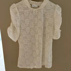 Vit spetsblus från Kappahl - Superfin vit blus från Kappahl i spets med blommigt mönster. Blusen har korta puffärmar och rund halsringning. Perfekt för dig som gillar romantisk och feminin stil. Materialet är mjukt och lätt, vilket gör den skön att bära.