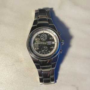 Casio Edifice silverfärgad klocka - Snygg Casio Edifice klocka i silverfärgat rostfritt stål med svart urtavla och kronograf-funktion. Klockan har datumvisning, tre subdials och ett robust armband med Casio-logga på spännet. Rund boett och stilren design som passar till många outfits.