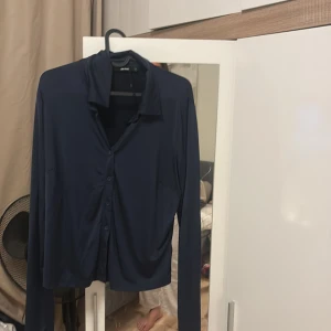 Mörkblå skjorta från Offcode - Mörkblå skjorta från Offcode med klassisk krage och knäppning framtill. Skjortan har lång ärm och är tillverkad i ett mjukt, tunt material som ger en snygg och avslappnad look. Perfekt för dig som gillar stilrena plagg med enkel design.