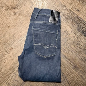 Replay Anbass jeans mörkblå W31 L32 - Säljer ett par mörkblå Replay Anbass jeans med klassisk femficksdesign och snygga kontrastsömmar på bakfickorna. Jeansen har en slim passform och är tillverkade i mjukt denimtyg som sitter skönt hela dagen. Jeansen är i bra skick men har en defekt brevid bakfickan på första bilden. Nypris: 1699
