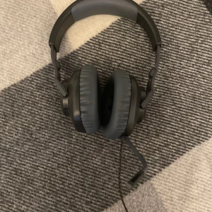 JBL QUANTUM 100 för gaming (svart) - Bekvämt over-ear spelheadset med kabel och justerbar mikrofon. Mjuka öronkuddar och vadderat huvudband för långvarig komfort. Passar perfekt för gaming och samtal. Ser ut att vara i gott skick utan synligt slitage.