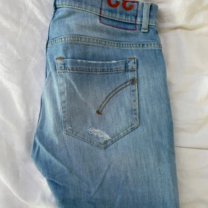 Ljusblå slitna jeans från Dondup - Ljusblå jeans med slitningar och broderade detaljer på bakfickorna. Klassisk femficksmodell med knapp och dragkedja. Jeansen har en rak passform och är tillverkade i mjukt denimtyg. Perfekta för en avslappnad och trendig look.