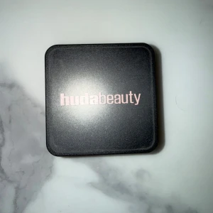 Huda Beauty Easy Bake löspuder Banana bread - Säljer ett Huda Beauty Easy Bake löspuder i en fyrkantig burk med svart lock och transparent underdel. Puderfärgen är ljusbeige och ger en matt finish. Perfekt för att sätta sminket och få en flawless look. Endast testad färgen passar nt mig 