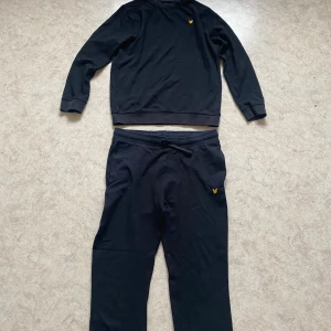 Svart sweatshirt från Lyle & Scott - Svart sweatshirt från Lyle & Scott med klassisk rund hals och gul logga på bröstet. Tröjan har långa ärmar och ribbade muddar vid ärmslut och nederkant. Perfekt för en chill och stilren look.