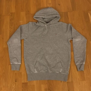 Grå hoodie från GANT med broderad logo - Grå hoodie från GANT med broderad logo på bröstet. Är S men passar XS. Klassisk känguruficka, snörning (lite slitna i endan) i huvan och ribbade muddar. Tillverkad i mjuk polyesterblandning, perfekt för chill dagar. Snygg och enkel stil som funkar året runt. Pris går diskutera🙌