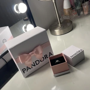 Pandora silverring med hjärta - Superfin silverring från Pandora med ett glittrigt hjärta i mitten och små stenar längs ringen. Kommer i originalask och presentbox med rosa rosett. Perfekt för dig som älskar söta detaljer och vill ha något extra på fingret.