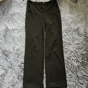 Svarta kostymbyxor från Vero Moda - Klassiska, högmidjade svarta kostymbyxor från Vero Moda med raka ben och midjehällor. Byxorna har diskreta fickor och stängs med dragkedja, hake och knapp. Perfekta för en clean och stilren look. Storlek S, säljer då jag inte kan ha de längre. De är lite slitna längst ner men det är ingenting man tänker på.
