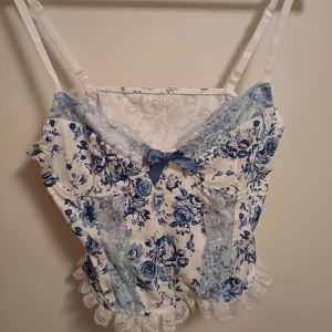 Blommig topp med spets och rosett - Supersöt topp med blått och vitt blommönster, ljusblå spetsdetaljer och liten rosett framtill. Justerbara axelband och volangkant i vit spets nedtill ger en romantisk vibe. Perfekt för dig som gillar vintage-inspirerad stil. Jag har aldrig använt men bara testat sett på den. Det står att det är storlek en men det är nog mer sx ❤️