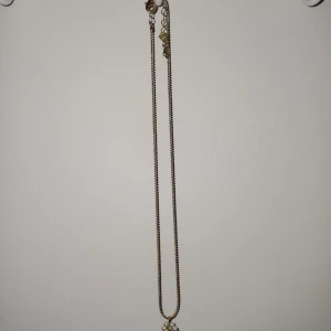 Guldfärgat halsband med pärlblomma - Snyggt halsband med guldfärgad kulkedja och ett hänge format som en blomma av vita pärlor och en guldfärgad pärla i mitten. Perfekt accessoar för att lyfta din outfit med en söt och trendig detalj. ❤️