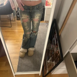 Levis 501 slitna blå jeans bootcut - Säljer ett par Levis 501 jeans i blå tvätt med slitna detaljer och stora hål på knäna. Modellen har klassisk femficksdesign, låg midja och bootcut-ben. Jeansen är i denim och har en avslappnad, vintage vibe. 