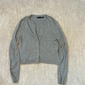 Grå kofta  - Grå kofta från 157 i storlek XS. Enkel och stilren design med rund halsringning, långa ärmar och knäppning framtill med matchande knappar. Tillverkad i mjukt material som passar perfekt för lager-på-lager under kyligare dagar.