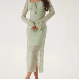 Ljusgrön spetsklänning med slits - Superfin ljusgrön långklänning i spets med långa ärmar och slits på sidan. Klänningen har en söt snörning framtill och är lätt transparent nedtill. Perfekt för dig som vill ha en romantisk och trendig look.