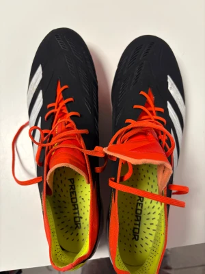 Adidas Predator fotbollsskor svart/silver - Säljer ett par Adidas Predator fotbollsskor med svart ovandel, silvriga ränder och detaljer i neonorange. Skorna har snörning, platt sula med fasta dobbar och insida i gulgrönt. Materialet är syntet och designen är sportig med Predator-logga på både insida och yttersula.     Använda av Allsvenska fotbollsspelare. 9/10 skick