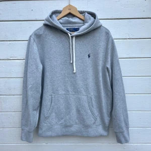 Grå Ralph Lauren Hoodie  - Snygg Ralph Lauren Hoodie i bra skick. Storlek L, passar som en M/L. Har en liiiten fläck på baksidan av ena ärmen uppe vid axeln, syns inte så tydligt i verkligheten eftersom den är på baksidan. Hör gärna av er vid funderingar🙌 Perfekt julklapp☃️