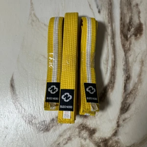 Gula Budo Nord bälten 320cm/240cm - Säljer två gula Budo Nord bälten med vita ränder, tillverkade i 55% bomull och 45% polyester. Bältena har broderad logga och är perfekta för kampsport. Längderna är 320cm och 240cm. Snyggt och slitstarkt material.