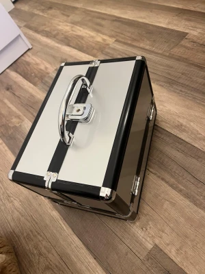 Smycke förvaring  - Säljer en stilren svart och silver smycke förvaring  i hårt material med metallhandtag och lås. Aldrig använd. Smycke förvaringen har flera fack och insida i svart tyg, perfekt för att organisera dina prylar. Nyckel medföljer för extra säkerhet. Snygg och praktisk för dig som gillar ordning. Tveka inte på att höra av er vid några frågor💗