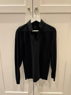 Svart henley från Massimo Dutti - Svart långärmad henley från Massimo Dutti med casual fit. Skjortan har en klassisk krage och knappar vid halsen. Tillverkad i mjuk bomull som känns skön mot huden. Perfekt för en clean och stilren look.