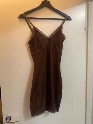 Brun ribbad spetsklänning H&M XS - Säljer en brun kortklänning från H&M i storlek XS. Klänningen är ribbad med tunna axelband och har fina spetsdetaljer längs urringning och nederkant. Den är figurnära och har en mjuk, stretchig känsla. Perfekt för dig som gillar en enkel men söt stil.